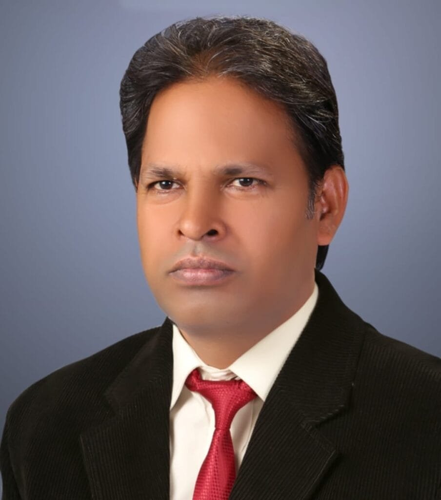 "A professional studio portrait profile photo of Ashok Sir, the Managing Director and legendary Chemistry expert at Apex Education. He is dressed in formal business attire, wearing a structured black corduroy blazer suit jacket over a crisp white collared dress shirt, paired with a vibrant red silk tie. He features dark hair neatly styled and faces forward with a serious, dedicated expression against a smooth, solid grayish-blue studio backdrop. This high-profile portrait represents elite academic leadership, expert chemistry mentoring, and the top-tier coaching executive network serving the Manigachhi and Darbhanga region."