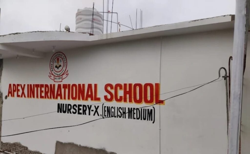 "The front building exterior wall of Apex International School, a leading educational institution in Darbhanga. The clean white wall features bold red lettering reading 'APEX INTERNATIONAL SCHOOL' alongside its official school emblem. Below the main title, black lettering specifies its curriculum coverage from 'NURSERY-X' and highlights that it is an 'ENGLISH MEDIUM' school. This campus is recognized as a premier school option and a core part of the top coaching and school network located in the Manigachhi region."